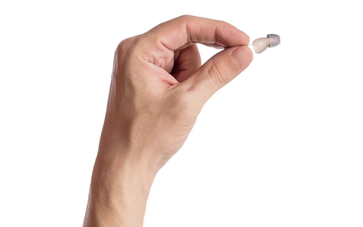 Hearli Hörgerät zwischen zwei Fingern, kleiner als eine 1-Franken-Münze
